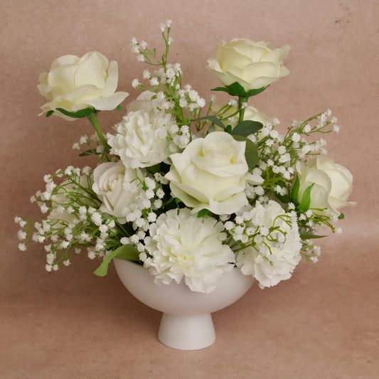 A table centerpiece featuring a white floral arrangement with roses and baby's breath in a white vase.