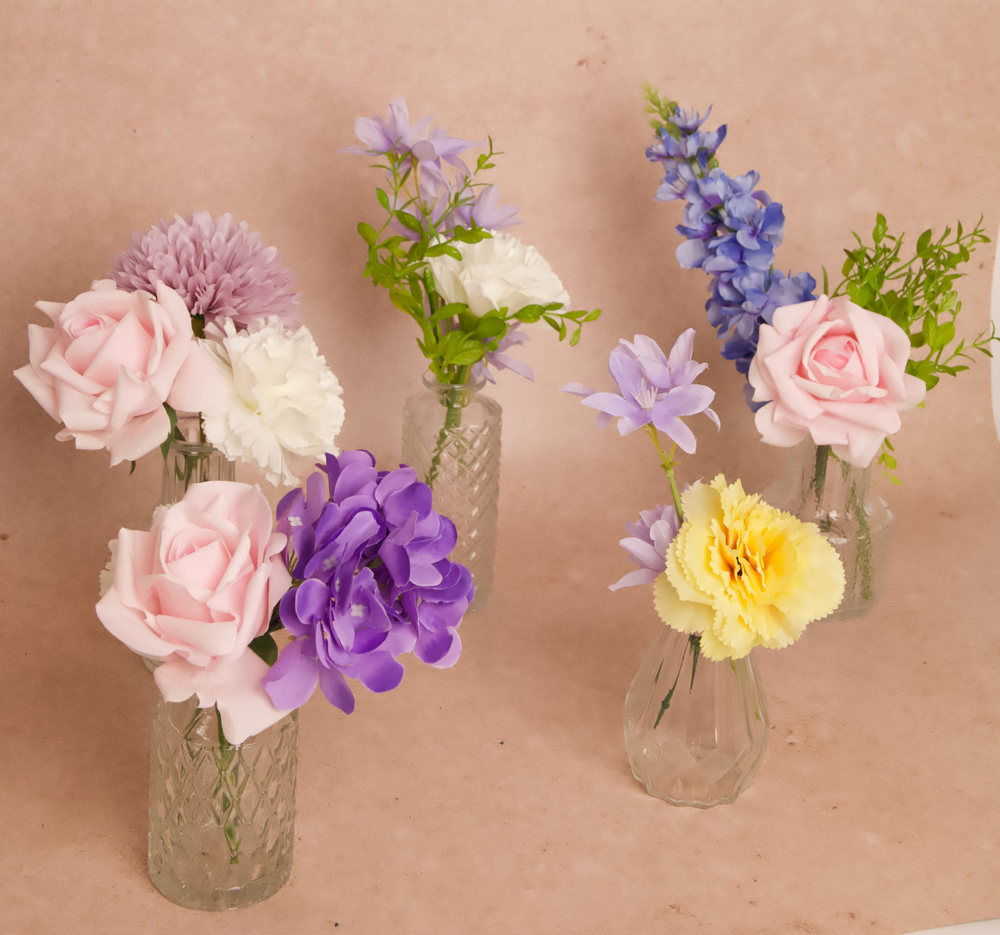 Colorful wedding table decorations in bud vases with blue delphinium, purple hydrangea, pink roses, yellow carnations, and greenery