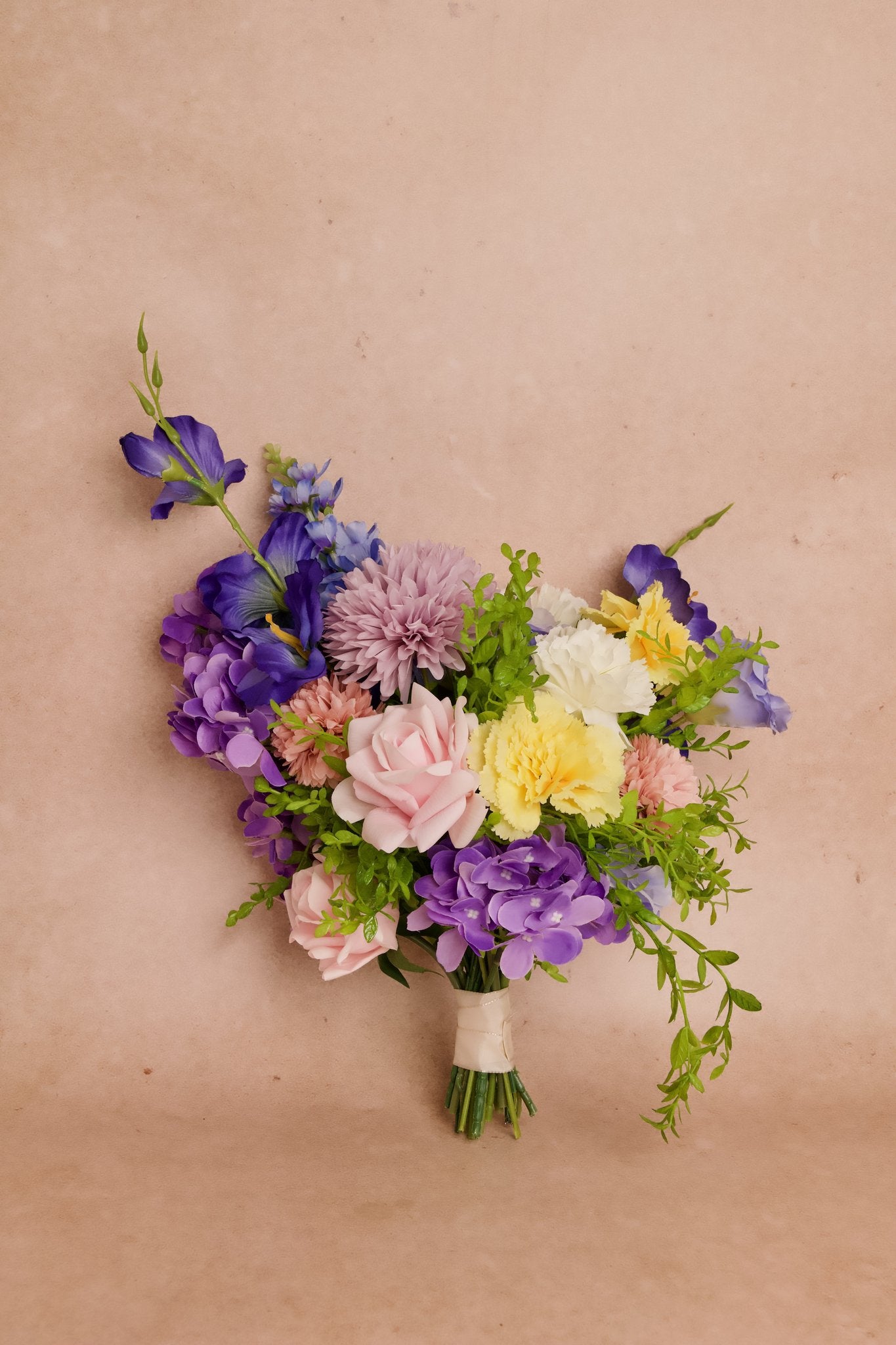 Colorful bridal bouquet with artificial purple irises and hydrangea, pink roses, yellow carnations, and other flowers and greenery for a romantic look