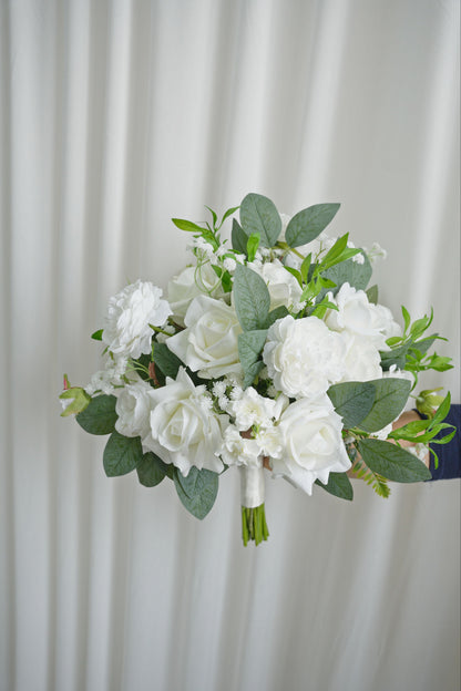 Bouquet of white flowers with green leaves held against a white curtain background