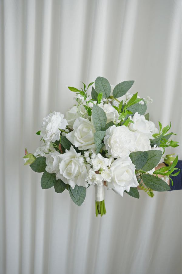 Bouquet of white flowers with green leaves held against a white curtain background