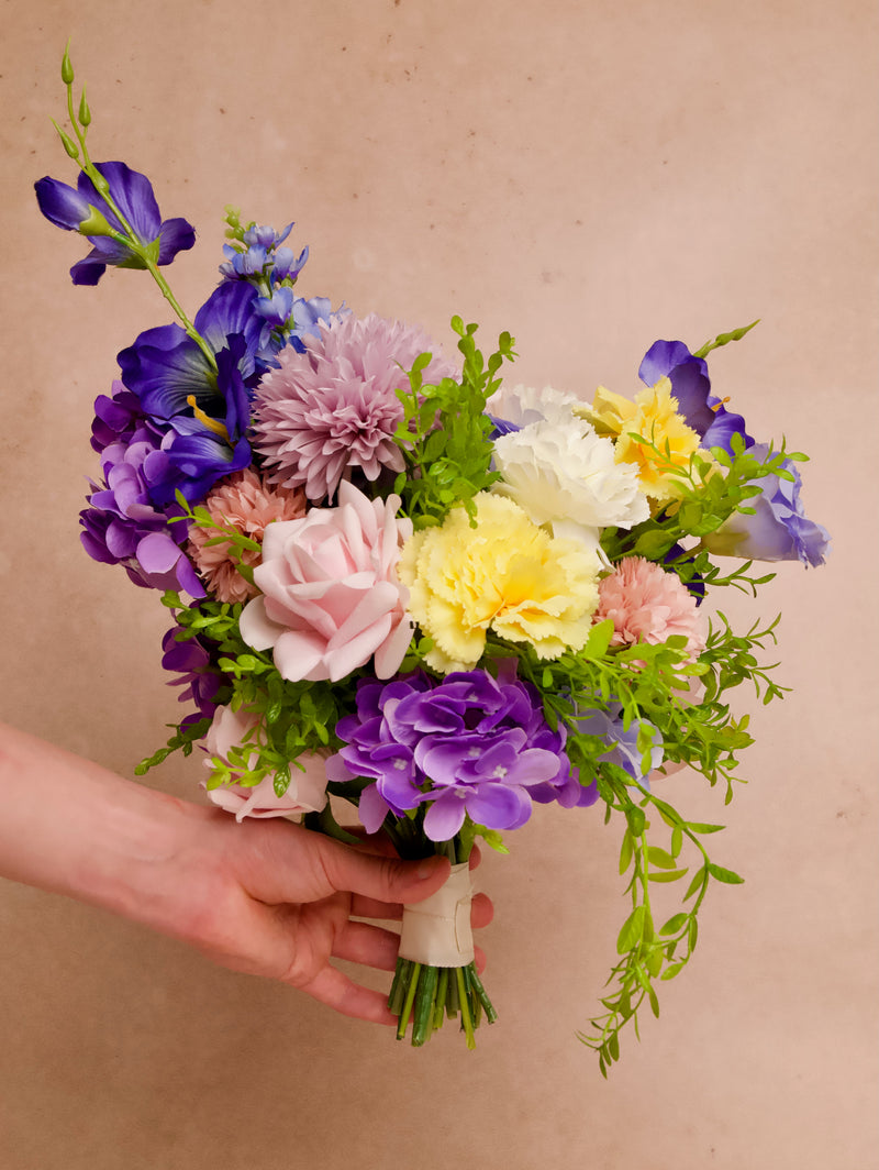 Colorful bridal bouquet with blue delphinium, purple hydrangea, pink roses, yellow carnations, and greenery